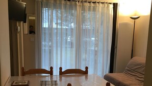 A dining area with a table and four chairs, a sofa, a standing lamp, and a window with curtains.