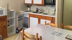 A compact kitchen with wooden cabinets, a microwave, a sink, and a dining area with a table and chairs.
