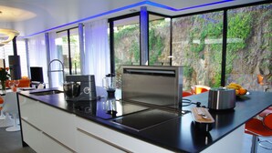 A modern kitchen with a black countertop, white cabinets, and a large window offering a view of greenery. - Villa Grand Standing 170m2 :4*, Pool & Jacuzzi PRIVATE: 5 Mn from the beaches (Perros-Guirec)