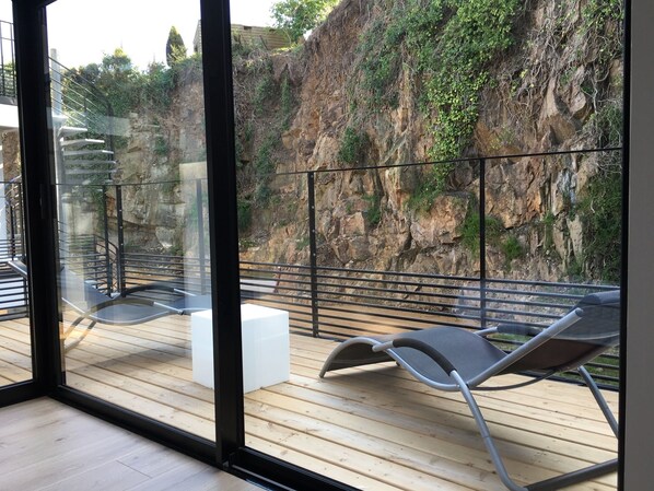 A balcony with a wooden floor, metal railings, and two lounge chairs.