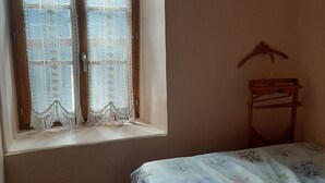 Een slaapkamer met een raam, een bed met bloemenbeddelsels en een houten stoel.