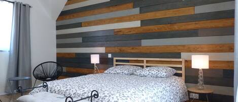 A bedroom with a bed, two bedside tables with lamps, a chair, and a window with curtains.