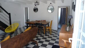 Un coin repas avec un sol à carreaux, une table en bois et des chaises. Deux miroirs sont accrochés au mur, et une lampe y est également fixée.