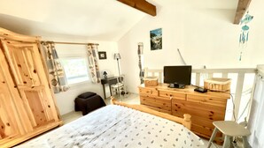 Une chambre à coucher comprenant un lit, une commode en bois, un bureau, une chaise et un téléviseur.