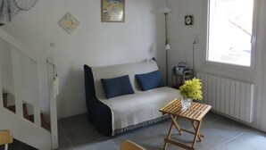 Un salon avec un canapé, une petite table sur laquelle est posée une plante, une affiche accrochée au mur et une fenêtre.