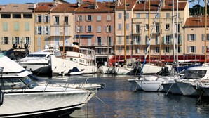 Un puerto deportivo con barcos amarrados, una torre del reloj y edificios con tejados de tejas rojas.