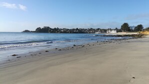 Une plage avec un ciel dégagé, une mer calme et une côte lointaine parsemée de bâtiments.
