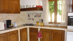 A kitchen with wooden cabinets, a gas stove, a coffee maker, and various utensils hanging on the wall.