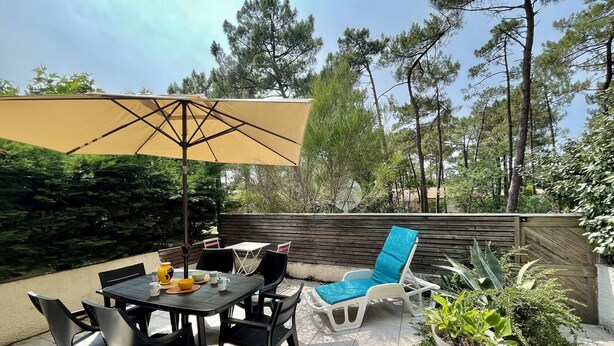 An outdoor patio with a table and chairs, a large umbrella, and potted plants.