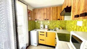 A compact kitchen with wooden cabinets, a microwave, a small refrigerator, and a green tiled backsplash.