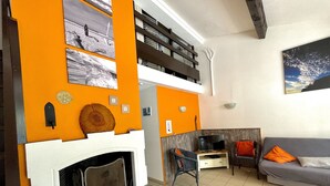 A living room with a fireplace, orange accent walls, a grey sofa, and a television.