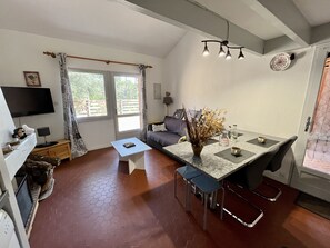 Un salon moderne comprenant un coin repas, un téléviseur à écran plat fixé au mur, un canapé, une table basse et une table à manger avec des chaises.
