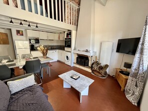 Ein modernes Wohnzimmer mit Sofa, Couchtisch und Essbereich mit Stühlen. Es gibt eine Küche mit Geräten und einen Kamin.
