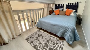 Una camera da letto con un letto, cuscini, un tappeto decorato, un comodino e vista attraverso una porta finestra.