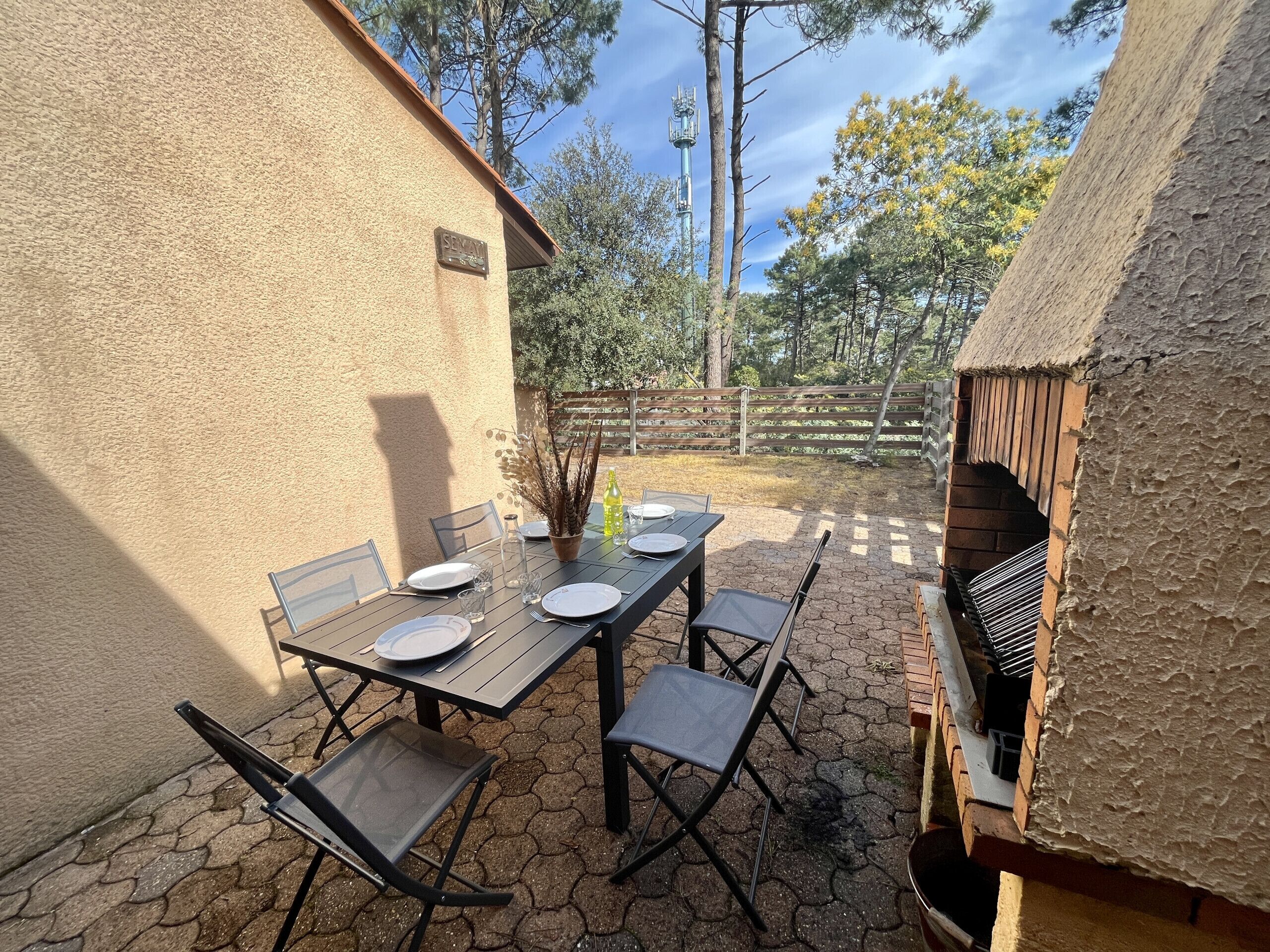 An outdoor patio with a table set for four, surrounded by chairs, a small potted plant, and a bottle.
