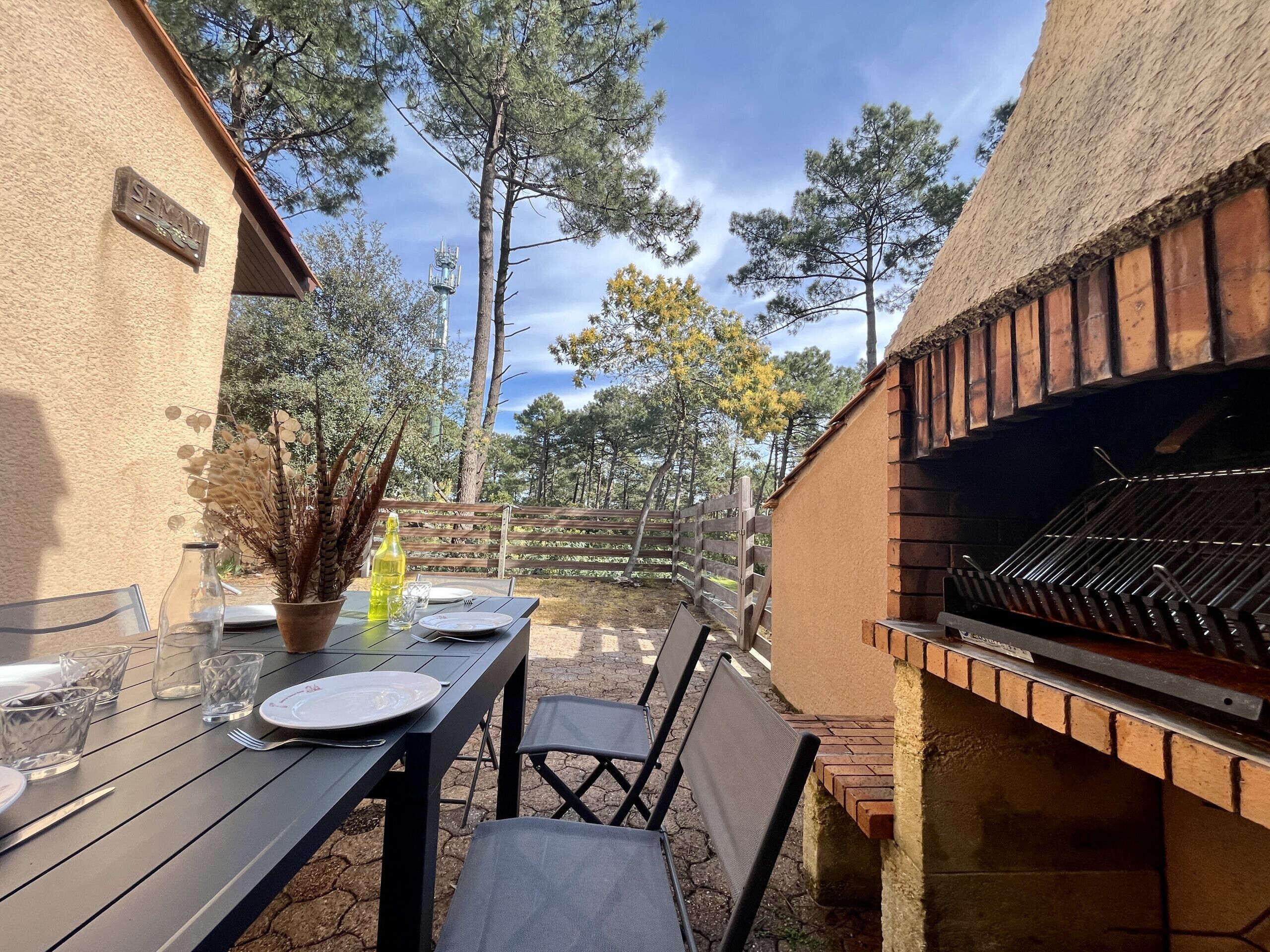 Een buitenpatio met een barbecue, een tafel gedekt met borden en bestek, en een potplant.