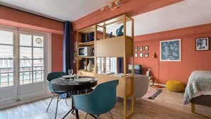 A modern living room with a dining area, a bookshelf, a television, and a bed.