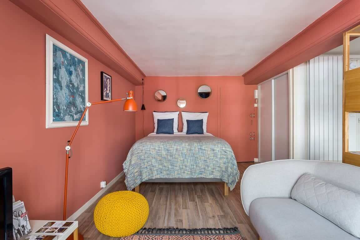 Ein Schlafzimmer mit einem Bett, einem Schlafsofa, einem gelben Pouf und Kunstwerken an der Wand.
