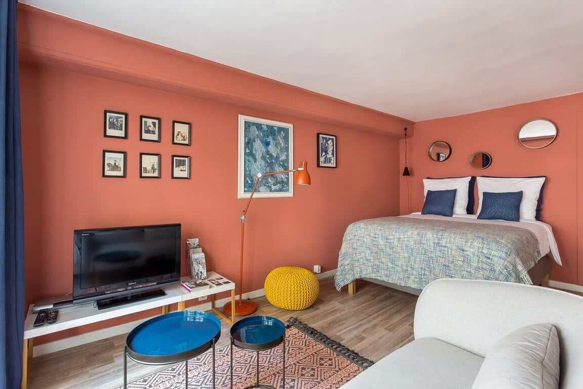 Ein Schlafzimmer mit Bett, Fernseher, Sofa, kleinem Tisch und Hocker in Gelb.