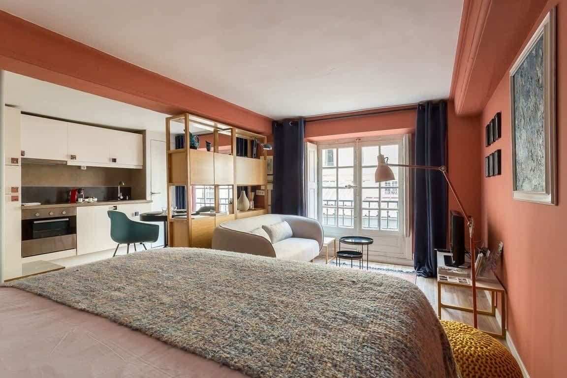 A modern hotel room with a large bed, a desk, a chair, and a balcony with a view.