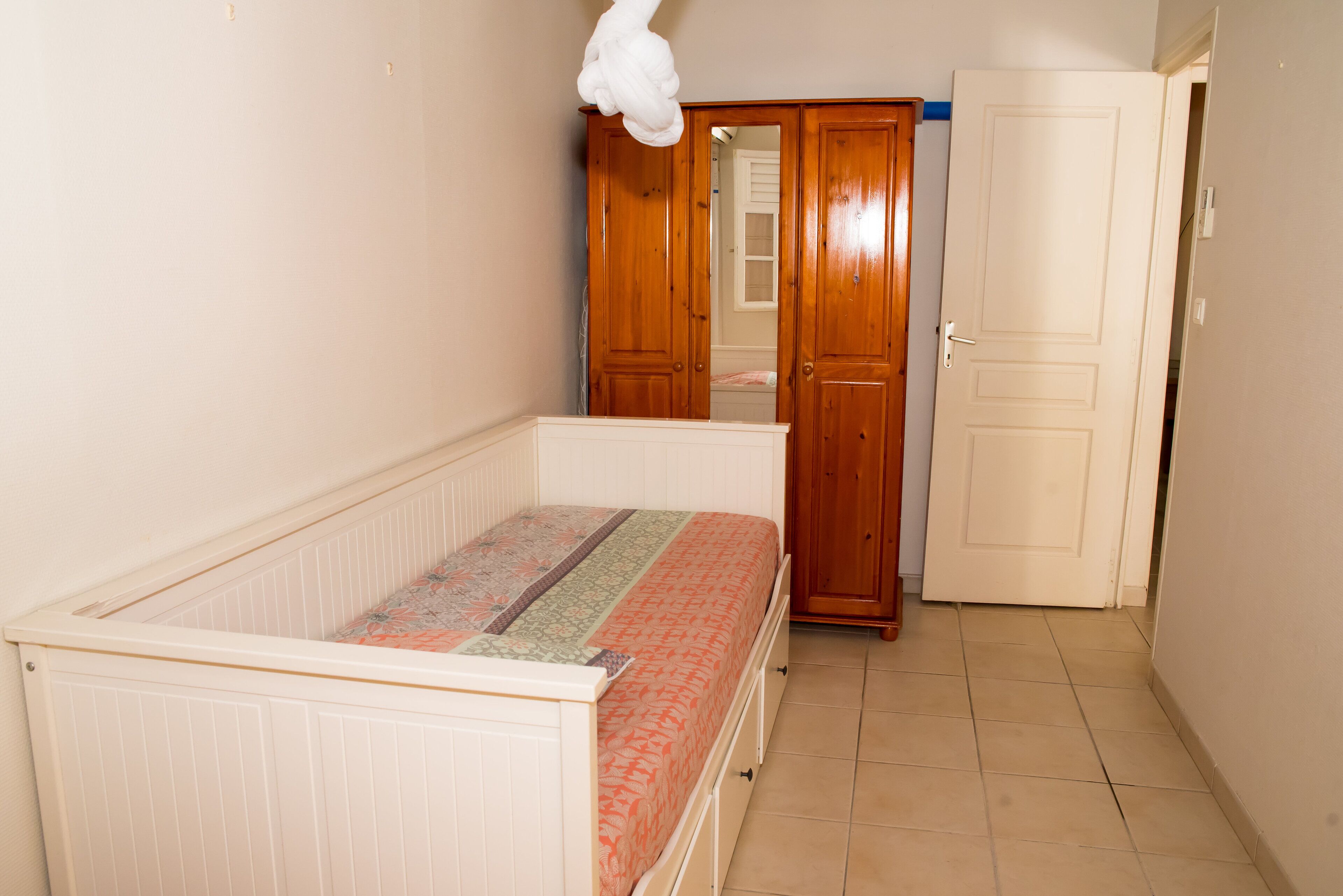 Een slaapkamer met een enkel bed, een houten kast en een witte deur.