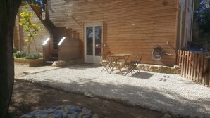 Une cabane en bois avec une terrasse en gravier, une plateforme en bois et un petit jardin.
