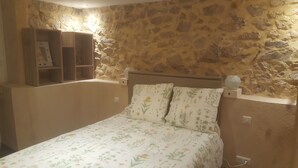 Une chambre avec un mur en pierre, un lit avec une literie à motifs floraux et une étagère en bois.