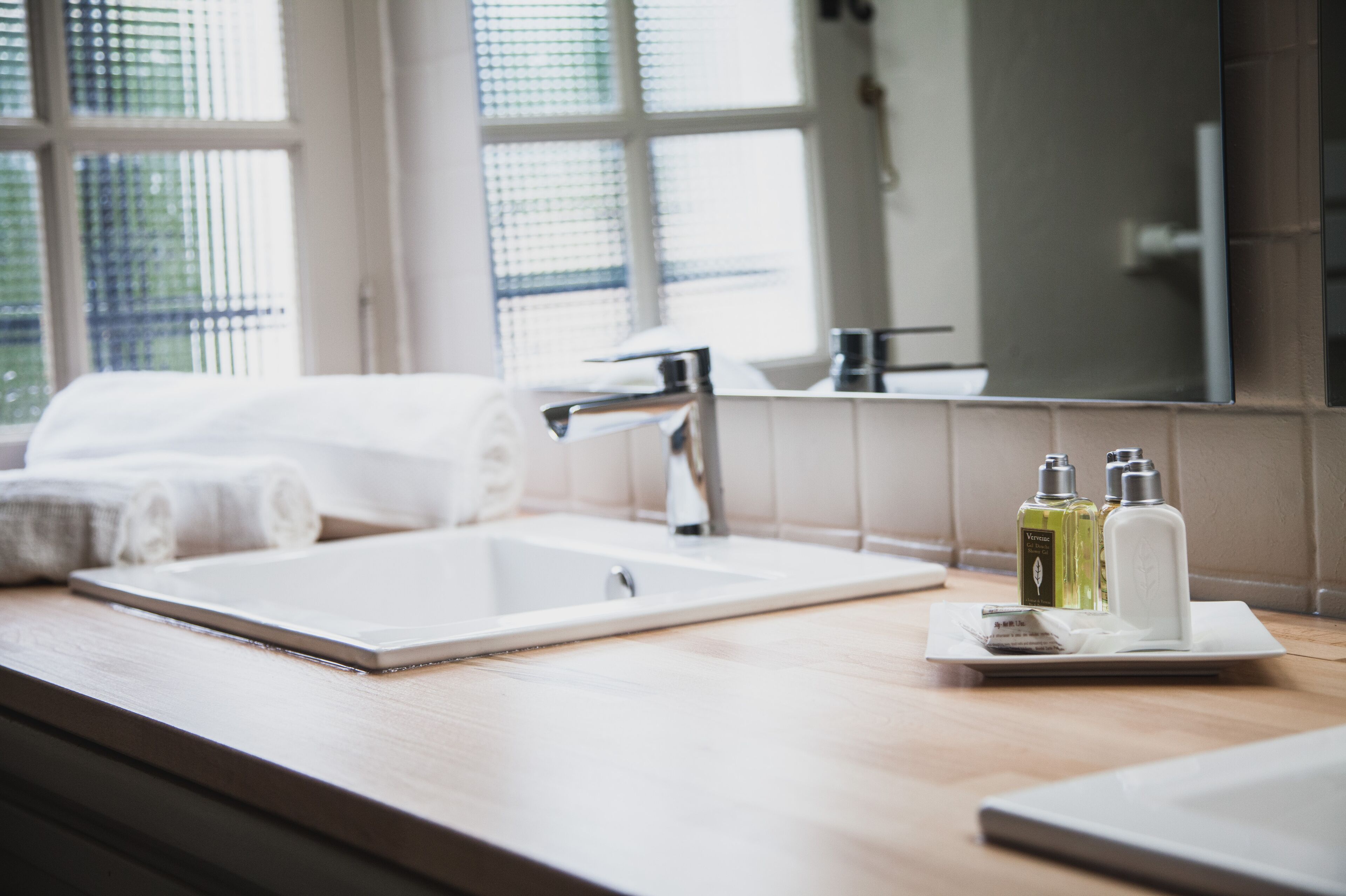 Une salle de bain avec un grand miroir, un lavabo et deux flacons de produits de toilette posés sur le comptoir.