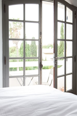 Ein Schlafzimmer mit einem großen Fenster und Blick auf eine Terrasse mit Stuhl und Tisch.