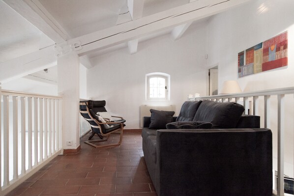 A spacious living room with a dark sofa, a rocking chair, and a window with natural light. - Magnificent VILLA IN PEACE in GRIMAUD, swimming pool, bowling alley: St Tropez, Ste Maxime (Grimaud)