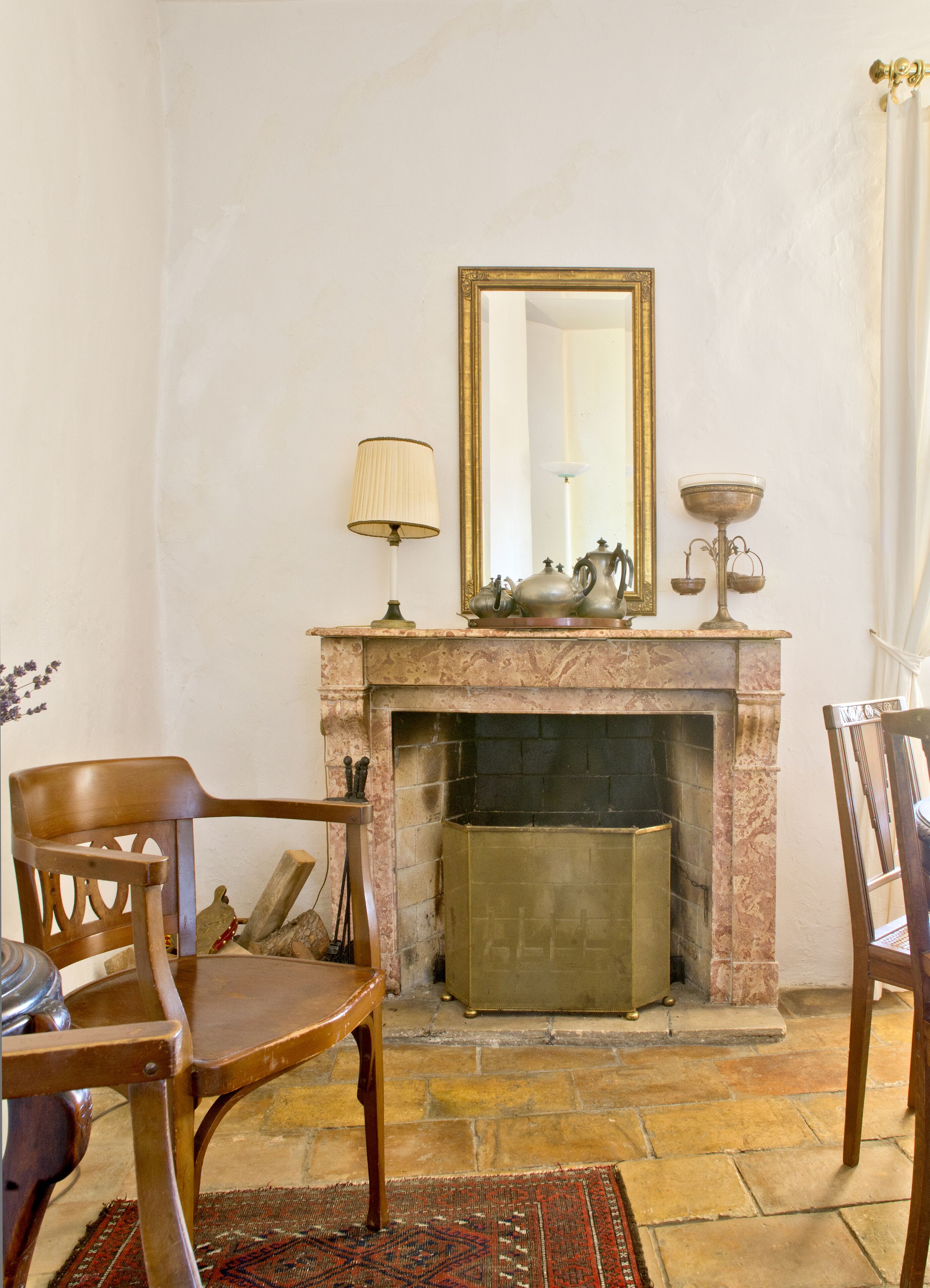 A room with a fireplace, a mirror, and two wooden chairs.