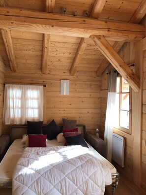 A wooden cabin bedroom with a bed, pillows, a window, and a radiator.