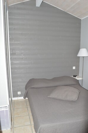 A bedroom with a bed, a nightstand, a lamp, and a wall-mounted outlet.