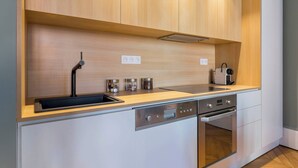 A modern kitchen with wooden cabinets, a stainless steel sink, a built-in oven, and a dishwasher. - Confort - Furnished apartment - Downtown Lyon (Lyon)