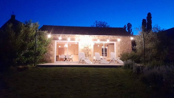 A stone house with a covered patio, outdoor seating, and a well-lit entrance.