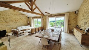 Un vaste espace dédié à la salle à manger, avec une longue table dressée pour le repas, un canapé et un mur en pierre en arrière-plan.