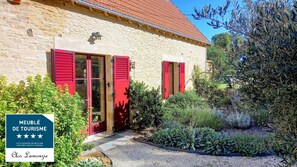 Un bâtiment en pierre avec des volets rouges et un jardin bien entretenu.