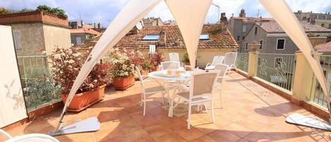 A rooftop terrace with a table and chairs, potted plants, and a view of the cityscape.