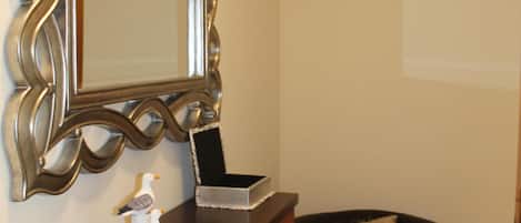 Una habitación con un aparador de madera oscura, un espejo con un marco ornamentado, un sillón de cuero negro y una pequeña figura decorativa de un pájaro.