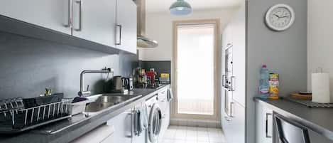 A modern kitchen with a washing machine, a sink, and a clock on the wall.
