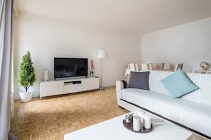 Una sala moderna con una televisión de pantalla plana, un sofá blanco, una mesita de centro y una planta en maceta.