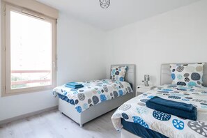 A bedroom with two beds, a window, and a bedside table with a lamp.