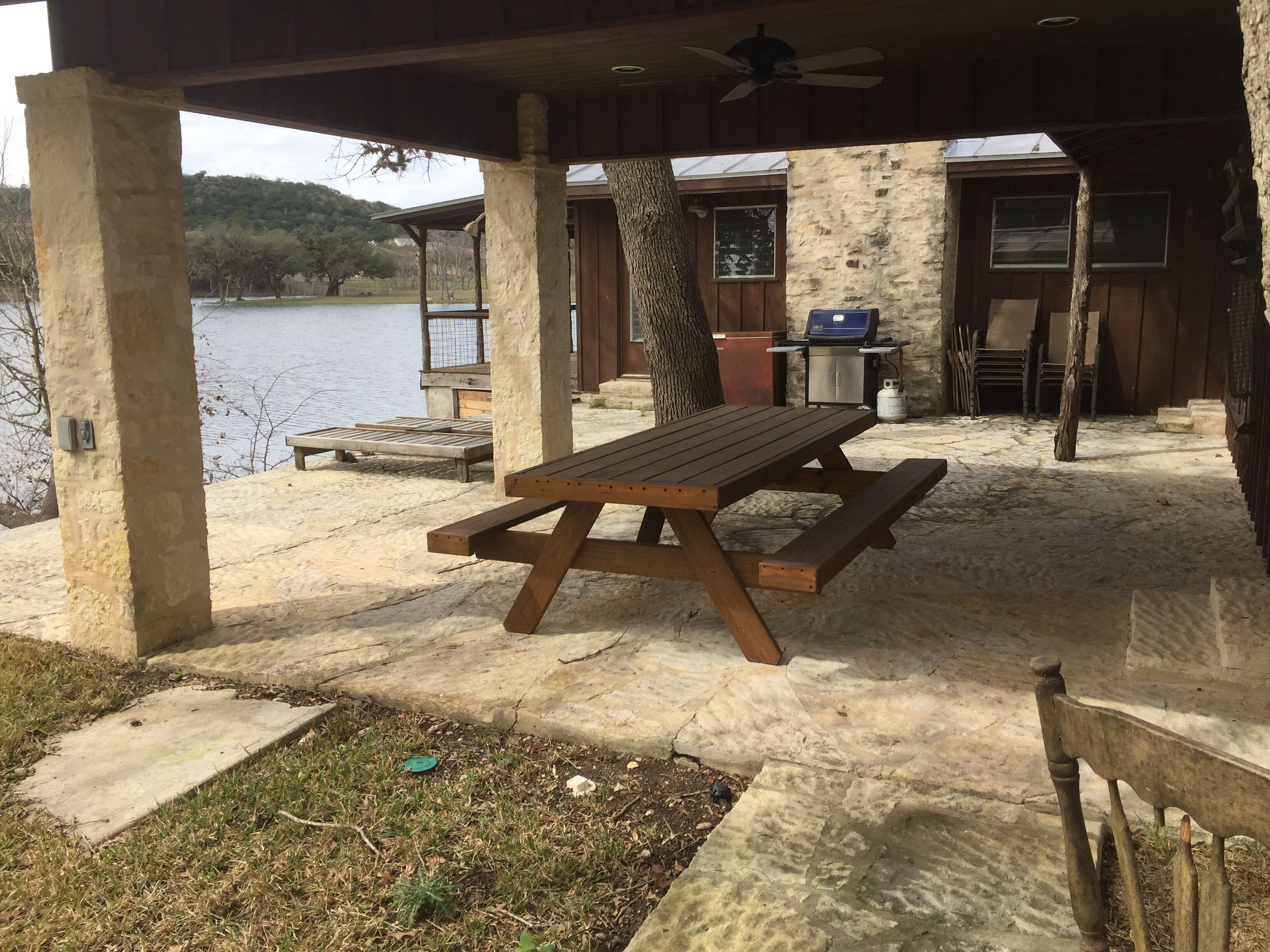 Zona de pícnic coberta amb taula i bancs de fusta, una barbacoa i vista a un llac.