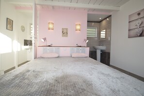 Un dormitorio con una pared de acento rosa, dos mesitas de noche con lámparas, una cama grande y una ventana.