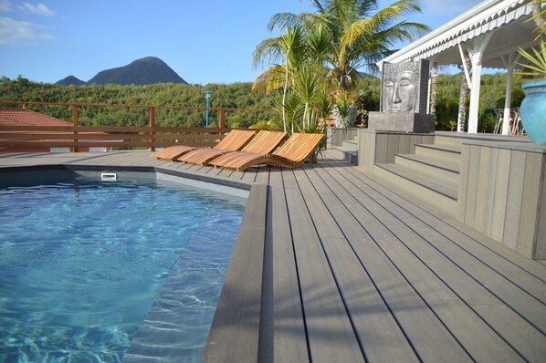 A pool area with wooden loungers, a stone statue, and a view of a mountain. - The spacious Villa Coconut, magnificent 180 ° view of the sea, the Rocher du Diamant (Le Diamant)