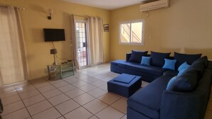 A living room with a blue sofa, a TV mounted on the wall, and a window with curtains.