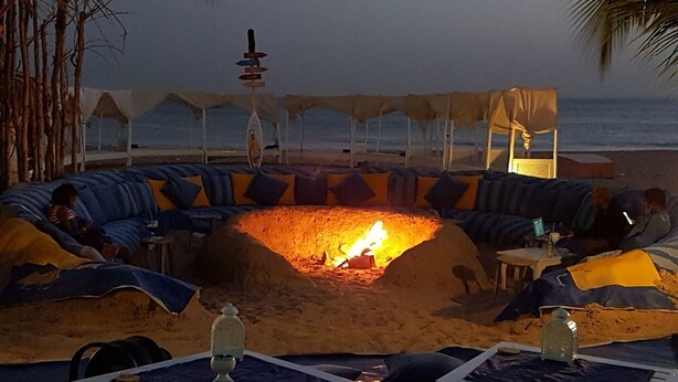 A beachside lounge with a central fire pit, seating areas, and tables.