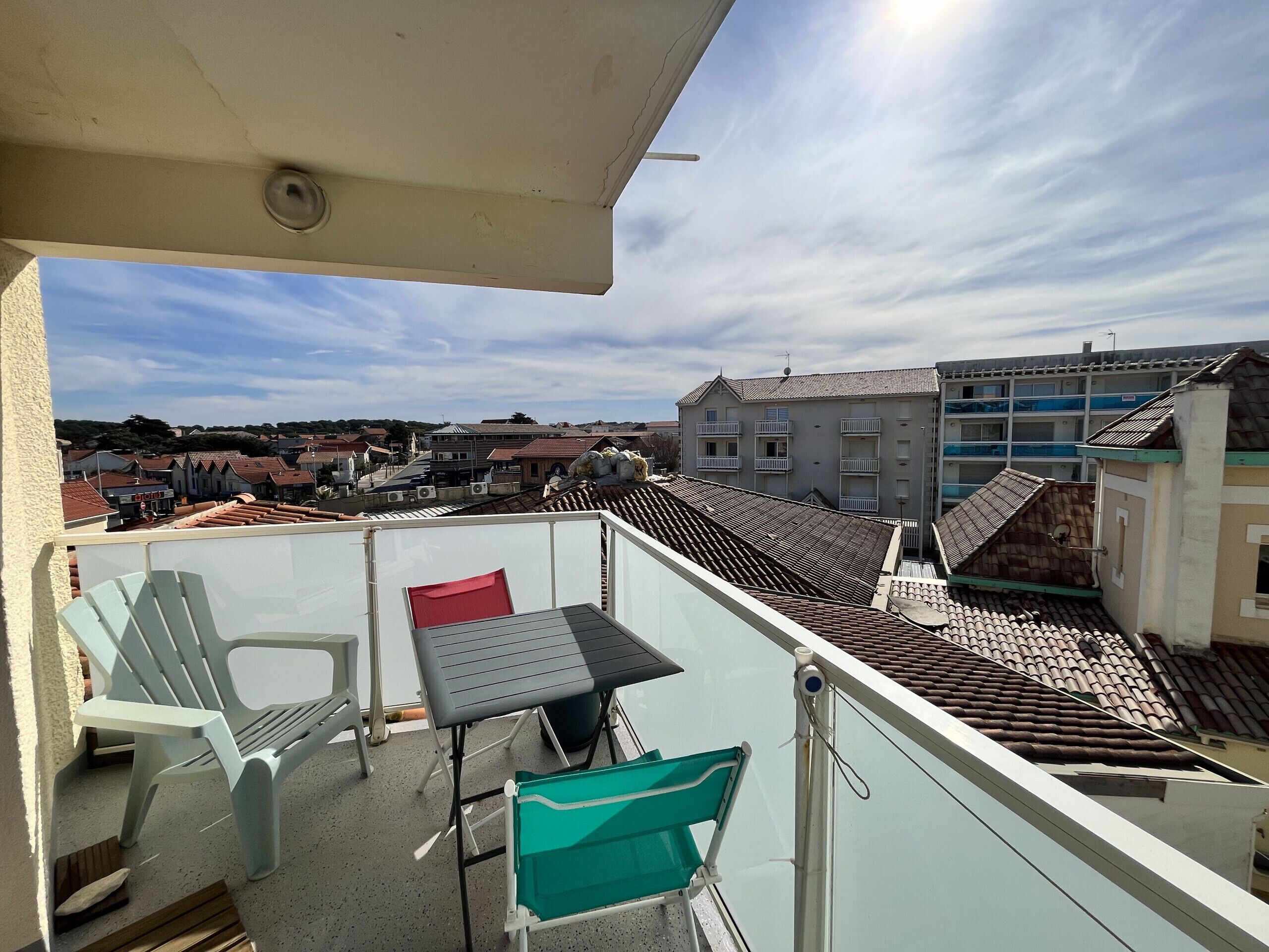Un balcon avec une table et des chaises, donnant sur un paysage urbain avec des bâtiments et un ciel dégagé.