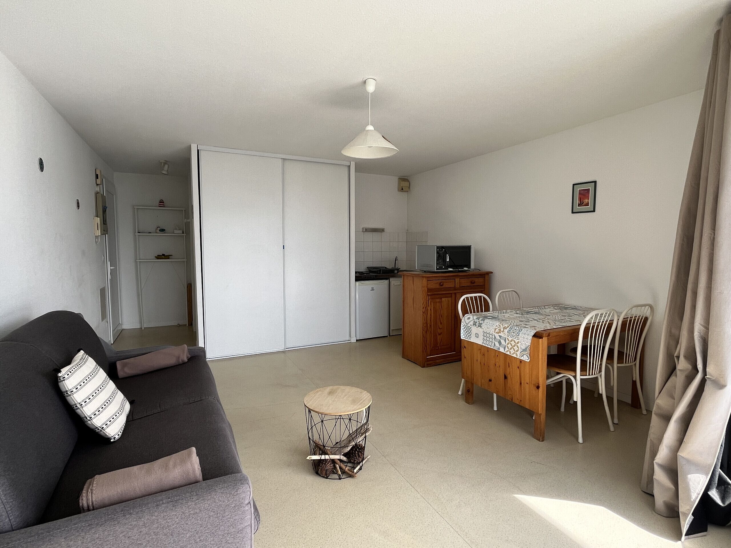 A compact living space with a sofa, a dining table with chairs, a kitchen area, and a small round table with a decorative item.