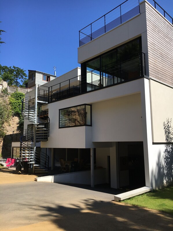 Un bâtiment moderne à deux étages, doté d’un balcon, d’un escalier en colimaçon et d’une grande fenêtre.